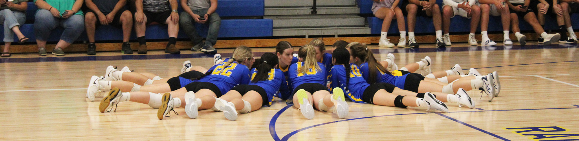 Girls volleyball team in a circle on the gym floor with coach