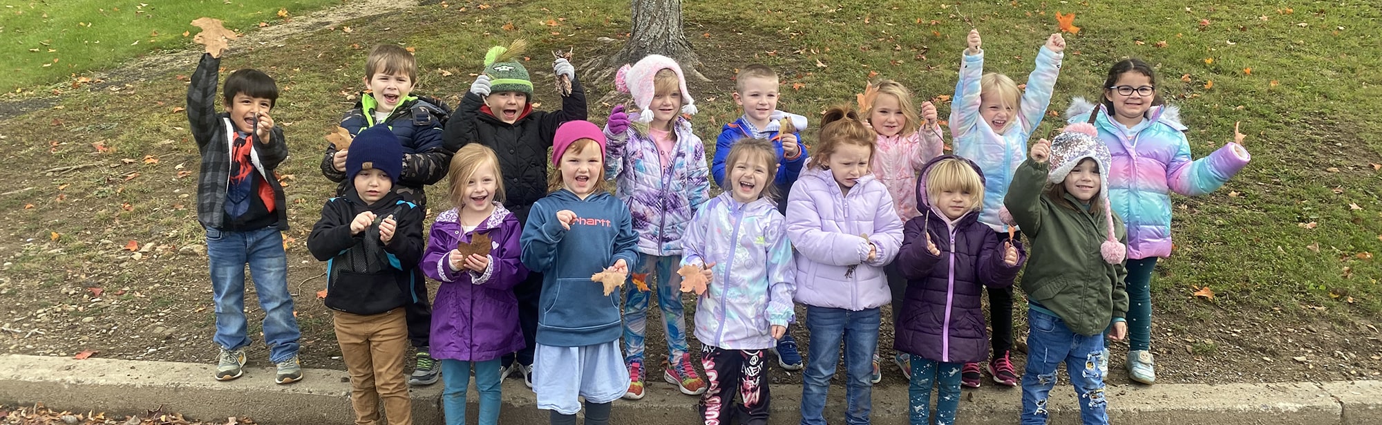 Group of happy preschool students outside holding up leaves