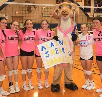 Girls volleyball team smiling next to ram mascot
